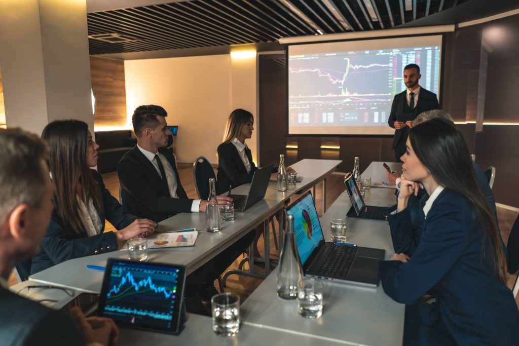 Ejecutivo presentando gráficos financieros a un comité de inversión en sala de reuniones.