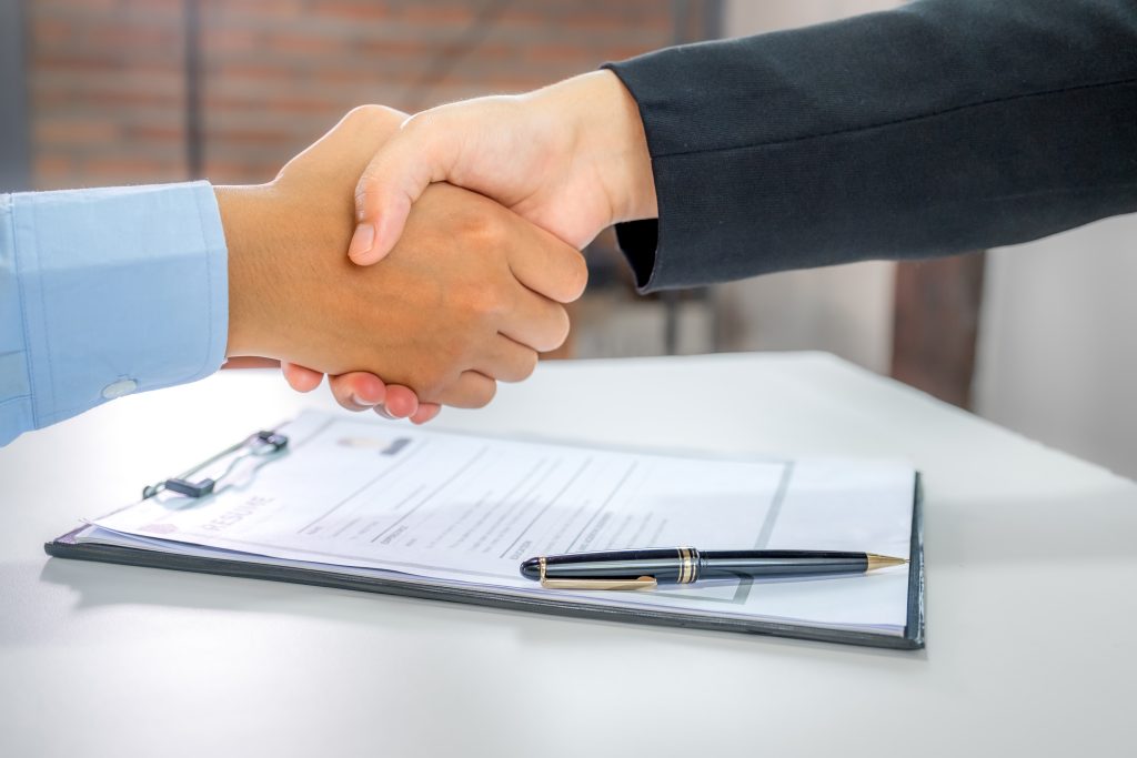 Dos ejecutivos estrechando la mano sobre documentación contractual tras un proceso de análisis de inversión.